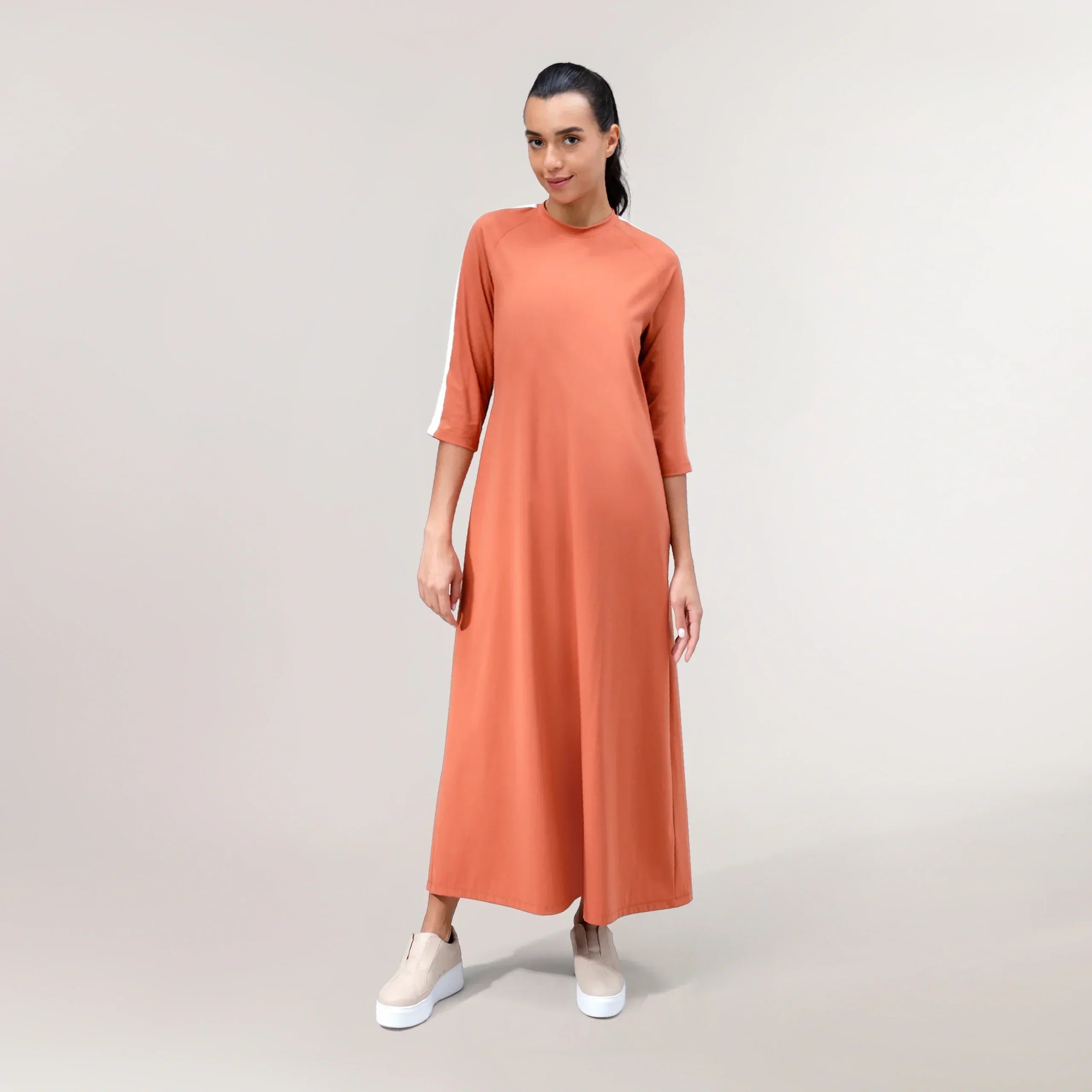 A model wearing a flared brick color maxi dress with a flowy hem - عارضة أزياء ترتدي فستان ماكسي واسع باللون الطوبي بحافة انسيابية
