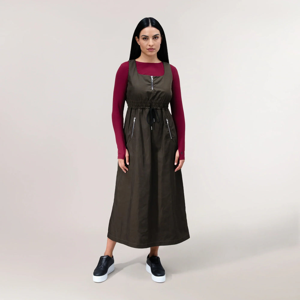 A model wearing a chocolate brown pinafore dress with wide straps & straight cut - عارضة أزياء ترتدي فستان بِنَافور بني شوكولاتة بحمّالات عريضة وقصّة مستقيمة