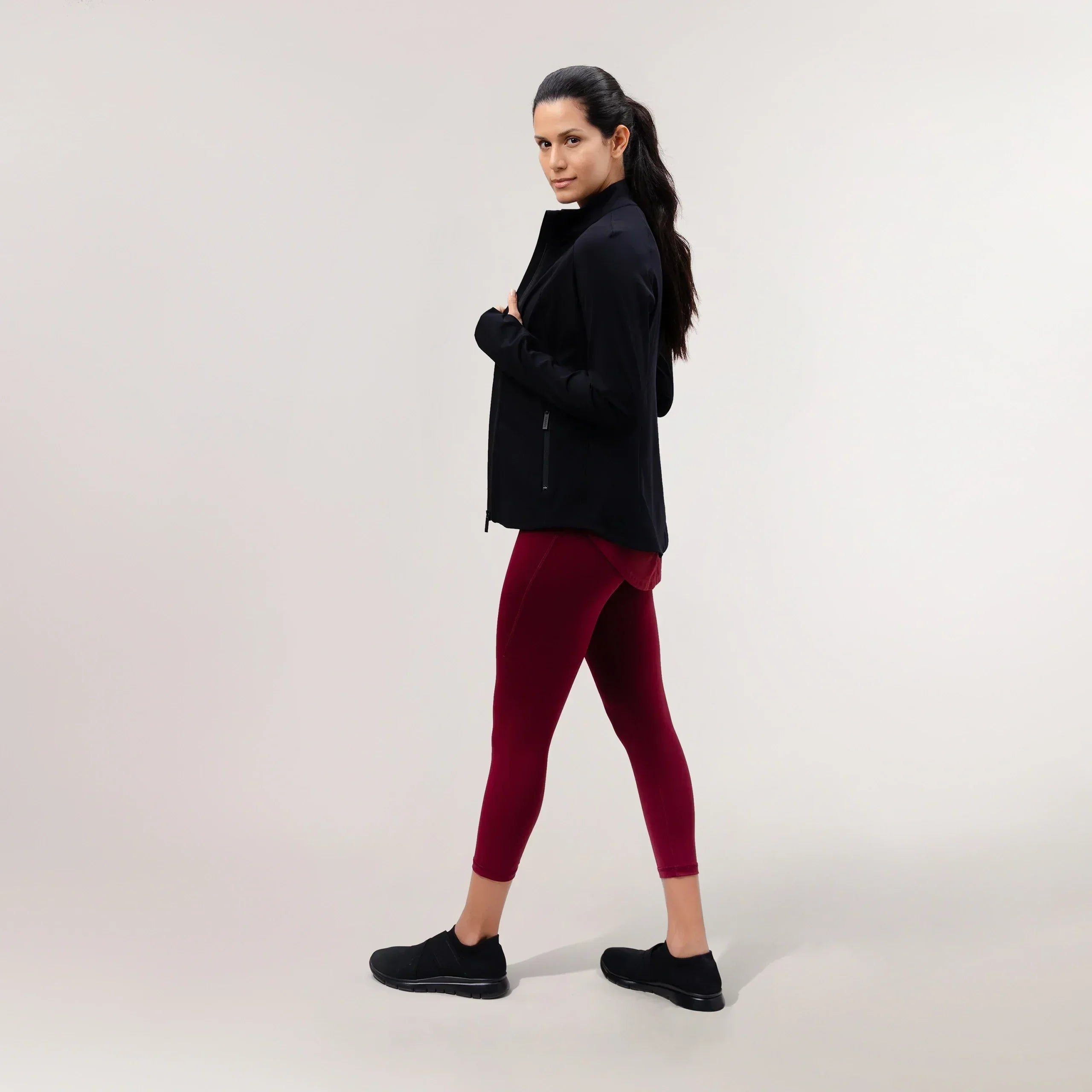 A model wearing a core black sculpting jacket over maroon leggings - عارضة أزياء ترتدي سترة مجسمة سوداء اللون فوق ليقنز كستنائي اللون