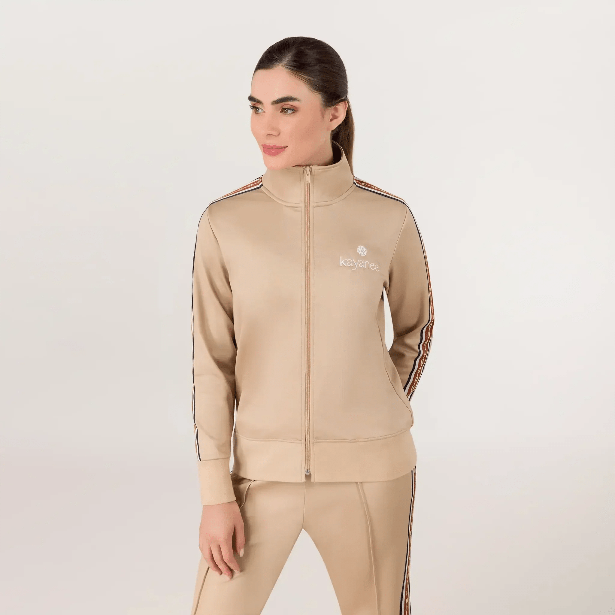 A model wearing a seasonal sand track jacket with Kayanee's logo - عارضة أزياء ترتدي سترة رياضية باللون الرملي تحمل شعار كياني