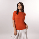 A model wearing a seasonal orange short sleeve knit sweater over a pleated skirt - عارضة أزياء ترتدي سترة برتقالية بأكمام قصيرة فوق تنورة بثنيات