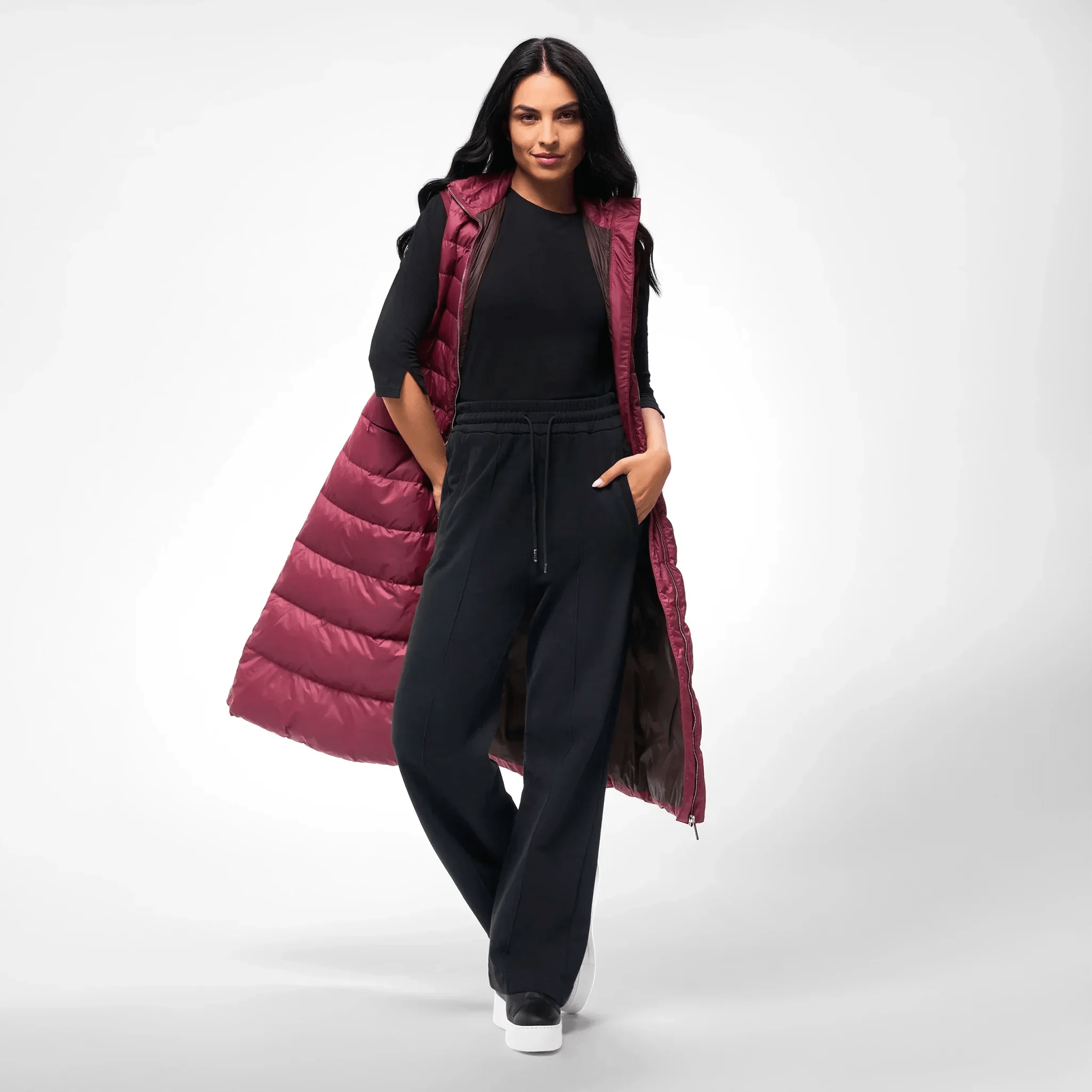 A model in a seasonal burgundy maxi puffer gilet over a black outfit - عارضة أزياء ترتدي سترة ماكسي منتفخة باللون العنابي فوق طقم أسود