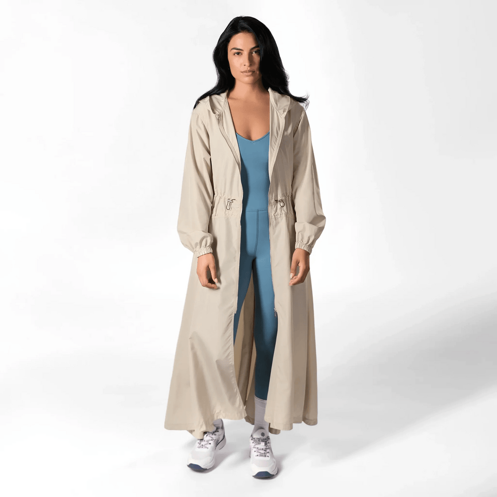 A model wearing a seasonal stone color hooded parka over a teal jumpsuit - عارضة أزياء ترتدي سترة باركا باللون الحجري بغطاء رأس فوق جمبسوت أزرق مخضر