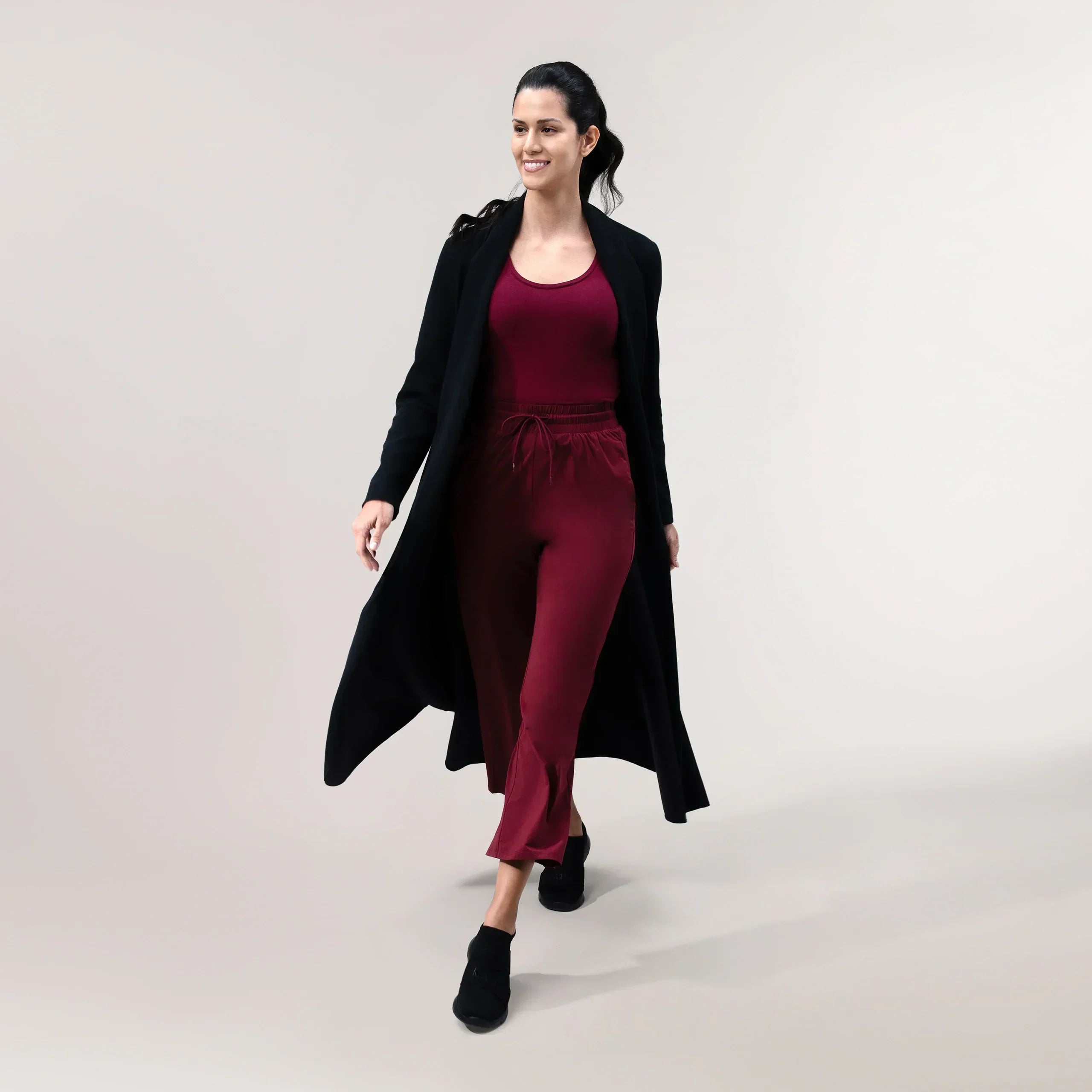 A model wearing a core black weekday coat over a maroon set - عارضة أزياء ترتدي معطف أسود يومي فوق طقم نبيتى اللون