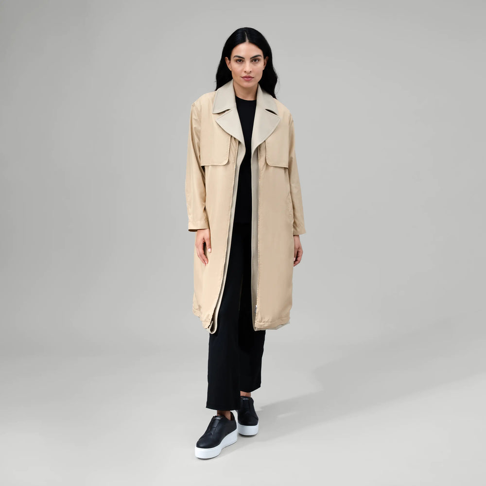 A model in seasonal beige gilet hybrid two piece trench coat - عارضة أزياء ترتدي معطف ترينش مكون من قطعتين باللون البيج