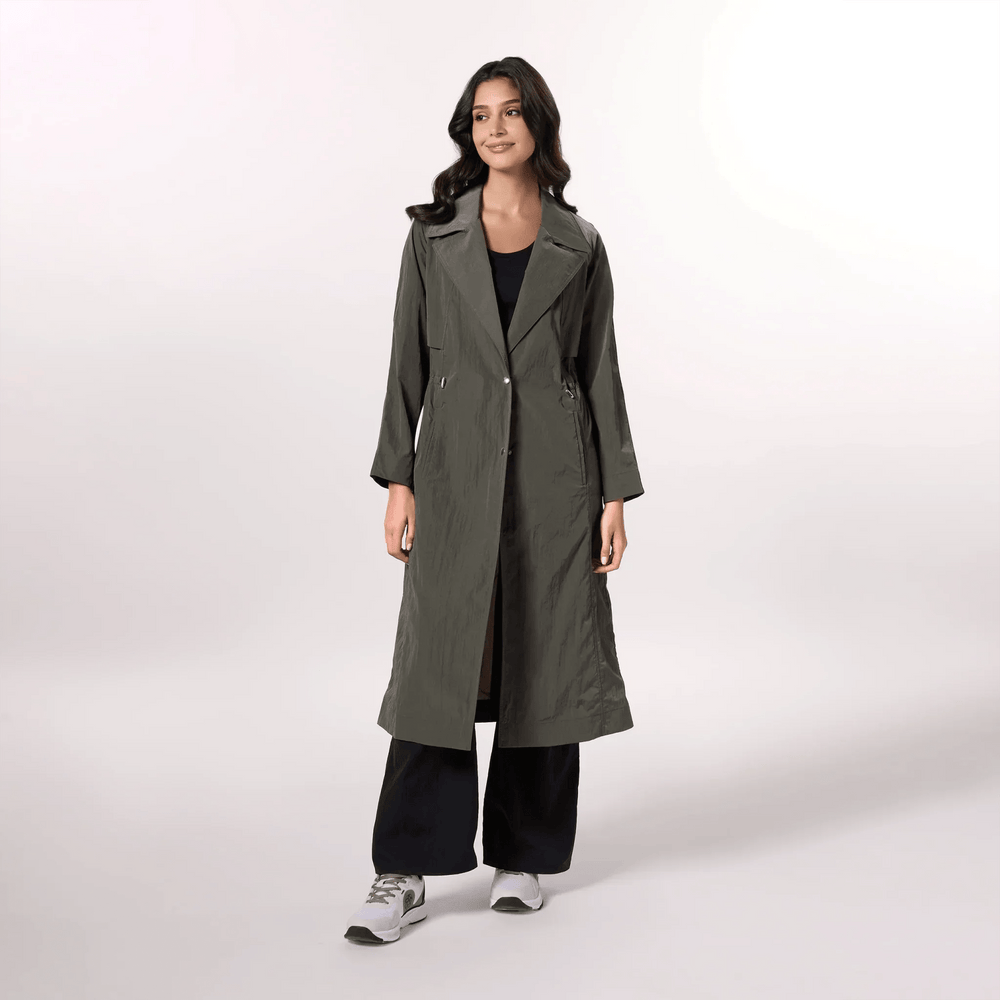 A model wearing an olive trench coat with a fluid silhouette & tie waist - عارضة أزياء ترتدي معطف ترينش باللون زيتوني بقصّة انسيابية وحزام ربط على الخصر