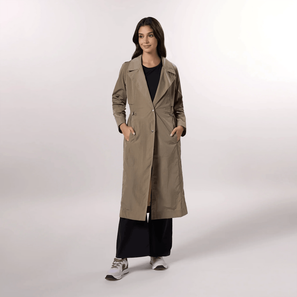 A model wearing a lightweight sand trench coat with a relaxed seasonal fit - عارضة أزياء ترتدي معطف ترينش خفيف الوزن باللون الرملي وقصّة موسمية مريحة