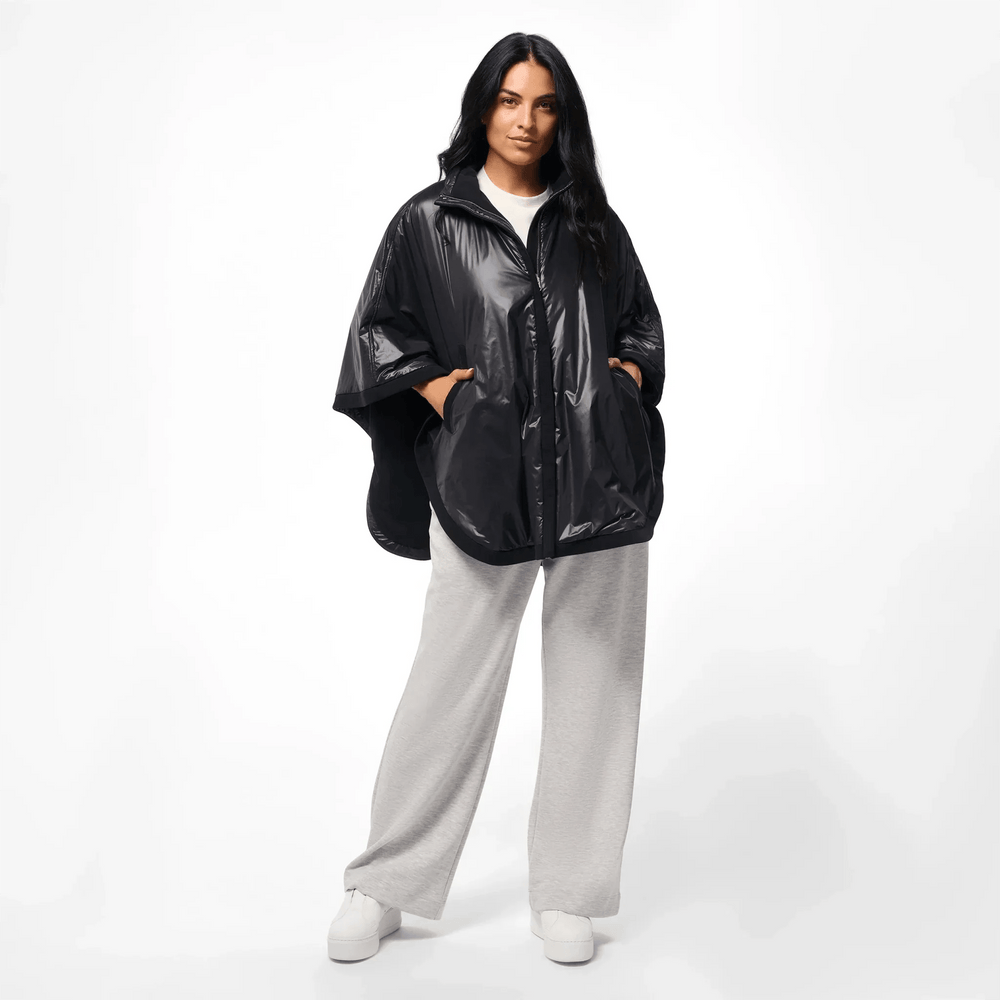 A model wearing a core black reversible cape over grey pants - عارضة أزياء ترتدي كاب قصير شتوي أسود بوجهين فوق بنطال رمادي