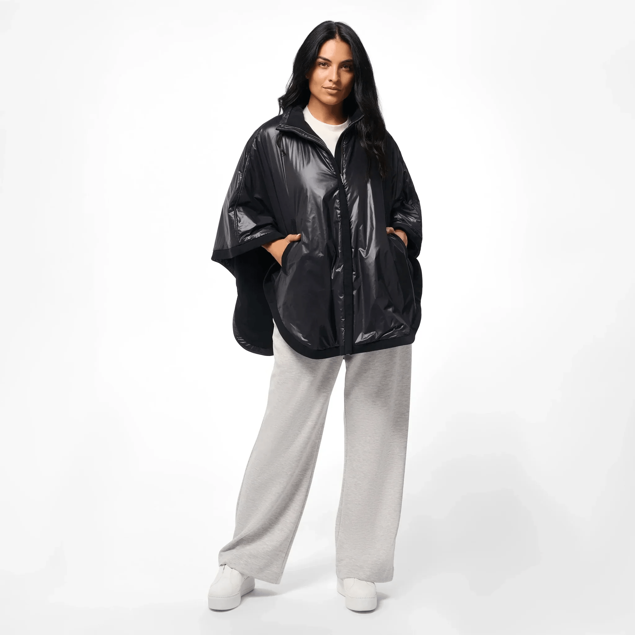 A model wearing a core black reversible cape over grey pants - عارضة أزياء ترتدي كاب قصير شتوي أسود بوجهين فوق بنطال رمادي
