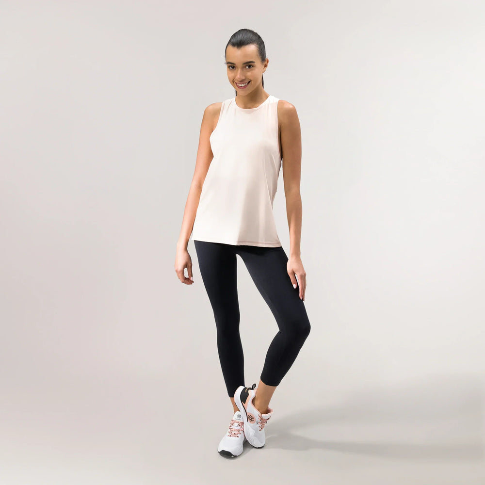 A model wearing a core light pink Twirl racerback top over black leggings - عارضة أزياء ترتدي بلوزة "تويرل" وردية فاتحة اللون بقصة دائرية فوق ليقنز أسود