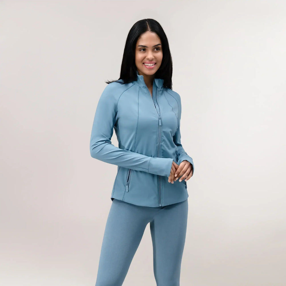 A model wearing a core blue sculpting jacket with front zip & side pockets - عارضة أزياء ترتدي سترة مجسمة باللون الأزرق مع سحاب أمامي وجيوب جانبية