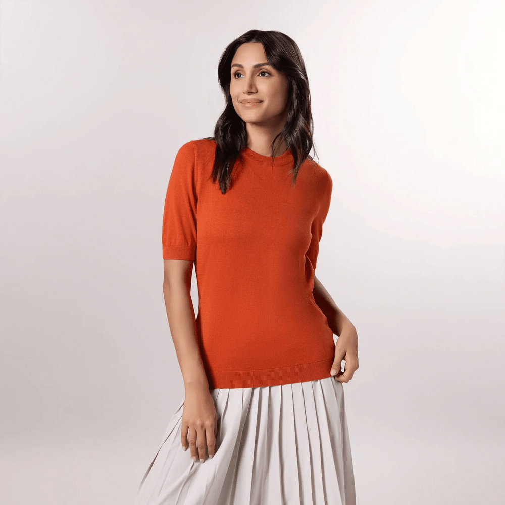 A model wearing a seasonal orange short sleeve knit sweater over a pleated skirt - عارضة أزياء ترتدي سترة برتقالية بأكمام قصيرة فوق تنورة بثنيات