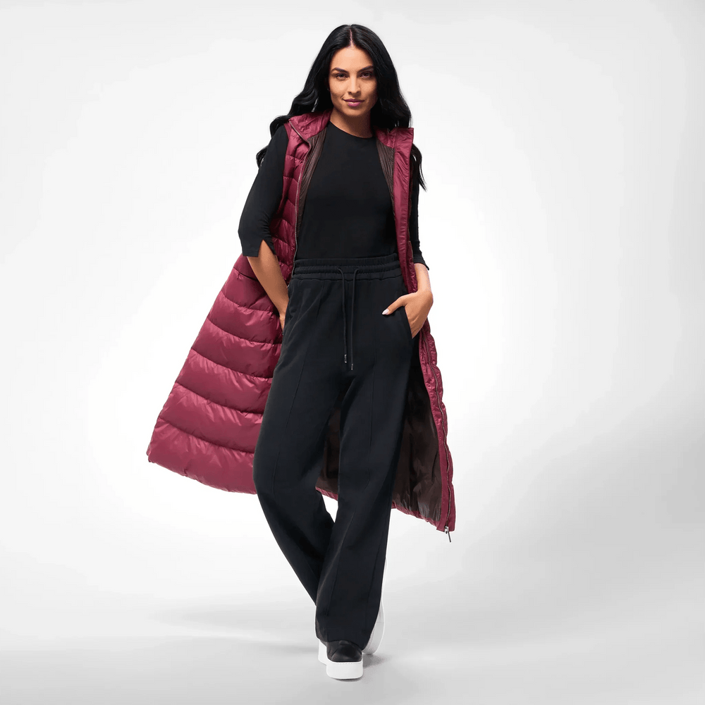 A model in a seasonal burgundy maxi puffer gilet over a black outfit - عارضة أزياء ترتدي سترة ماكسي منتفخة باللون العنابي فوق طقم أسود