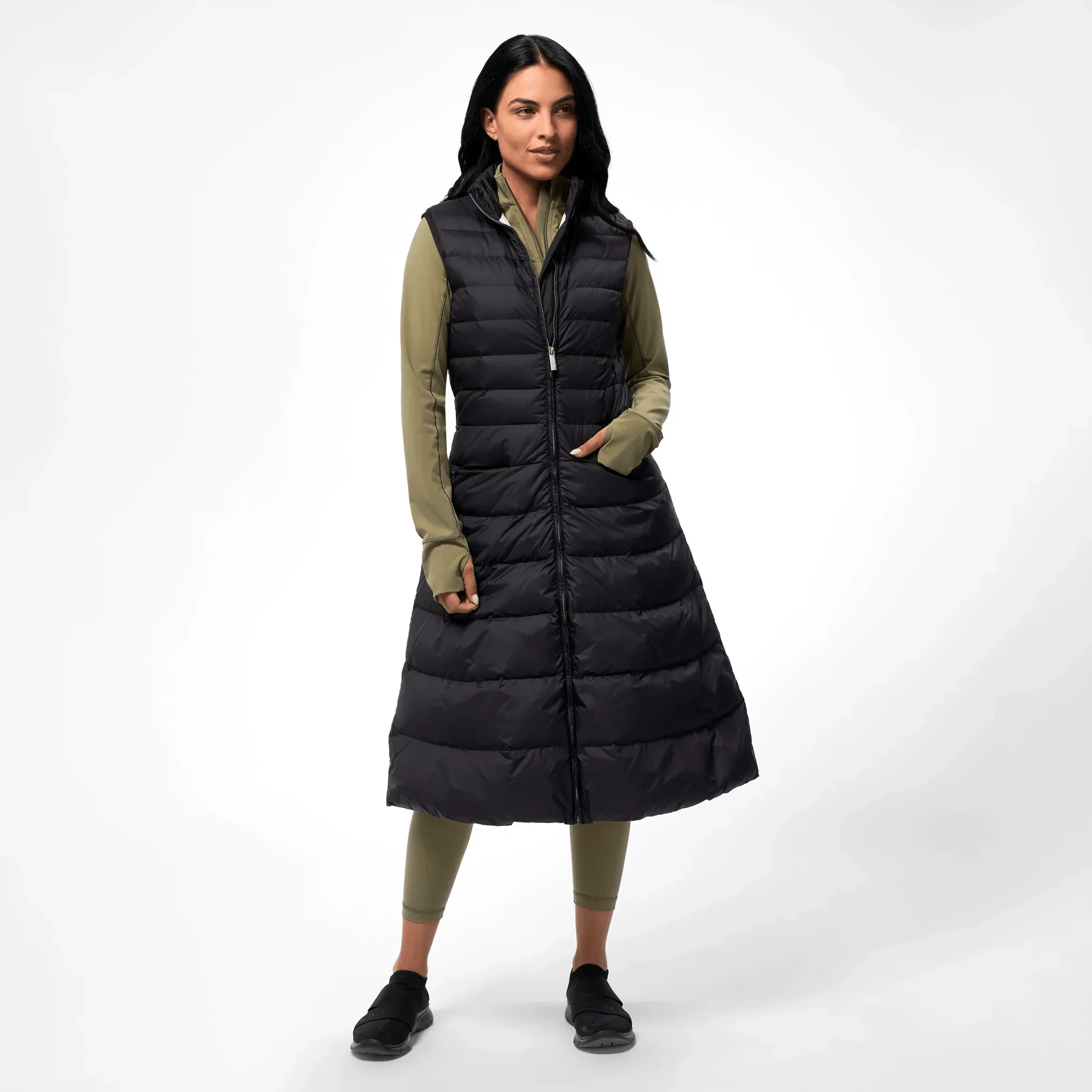 A model wearing a seasonal black maxi puffer gilet over a olive green set - عارضة أزياء ترتدي سترة ماكسي منفوخة باللون الأسود فوق طقم أخضر زيتوني
