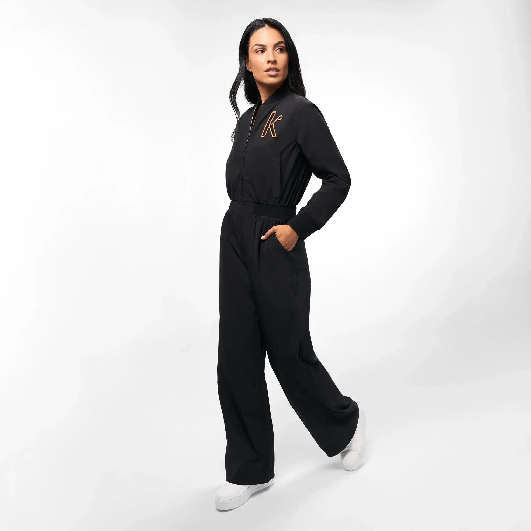 A model in a seasonal black utility jumpsuit with Kayanee's first initial on it - عارضة أزياء ترتدي جمبسوت سوداء مع الحرف الأول من اسم كياني عليها