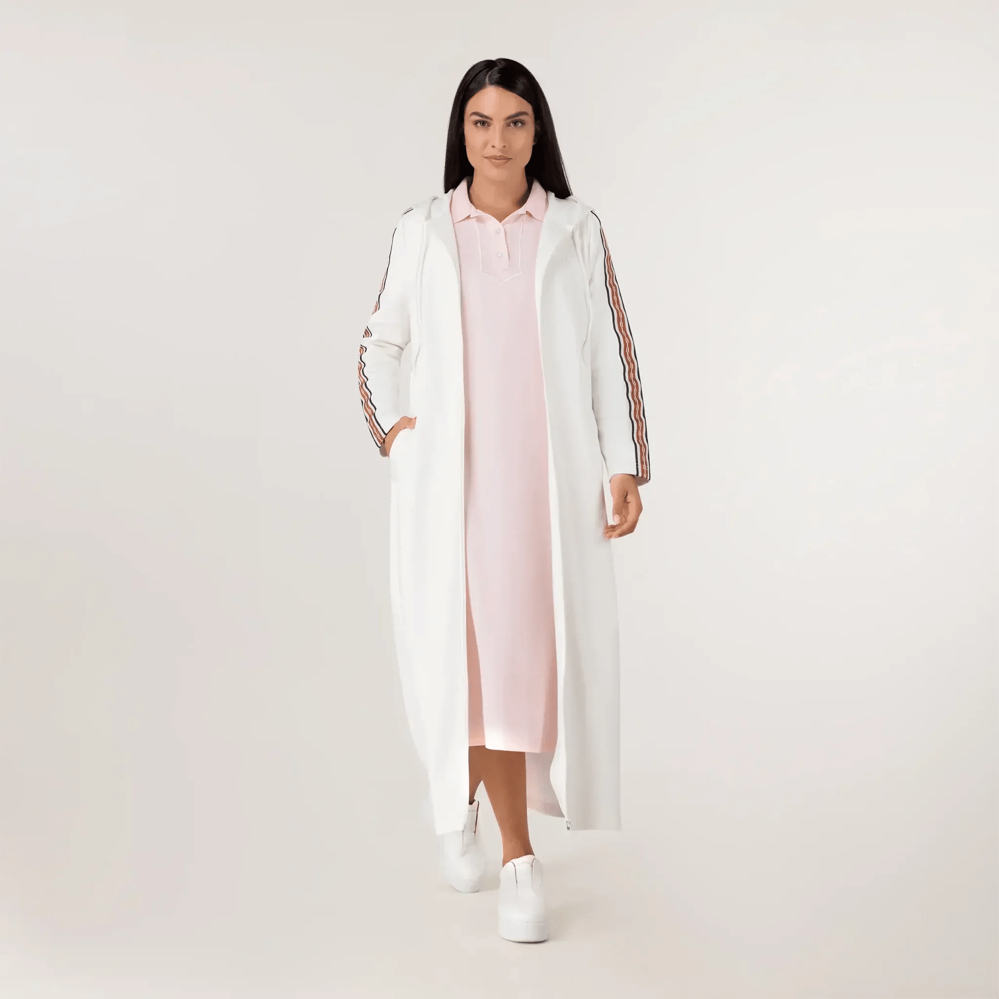 A model wearing seasonal white track abaya over a pink dress - عارضة أزياء ترتدي عباءة رياضية بيضاء فوق فستان وردي